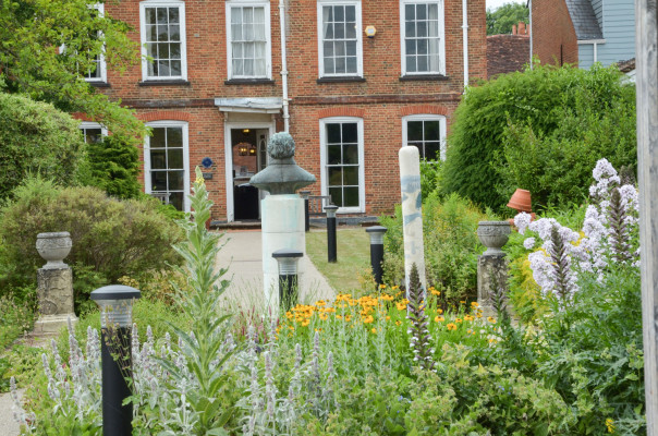 Back of red brick building, male bust in background, flowers in foreground.