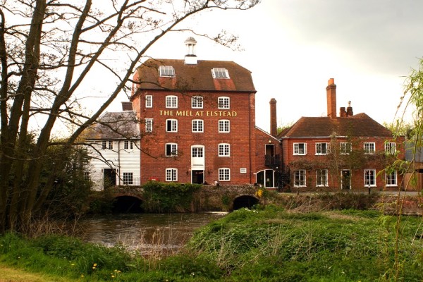 Large red brick building, river and grass surrounding.