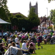 Crowd of people in park, with bandstand and gazebos.