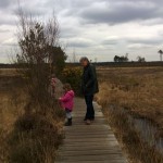 wooden boardwalk, moat on the right, grassland surrounding. Male and child on boardwalk.
