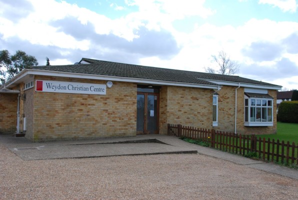 exterior of brick building, with wooden doors, fencing and grass to the right.