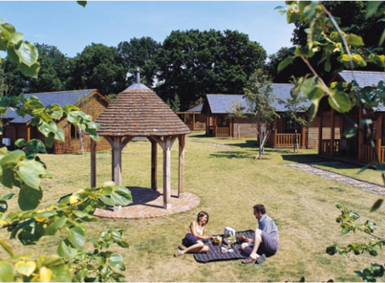 male and female having a picnic, wooden lodges in back ground