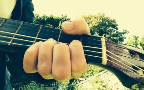 Hand, guitar neck, sky, trees.