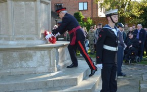 Male laying wreath on war memorial, group to the right watching, male in uniform in foreground