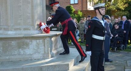 Male laying wreath on war memorial, group to the right watching, male in uniform in foreground