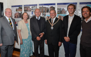 Six people standing in a row in front of an exhibition.