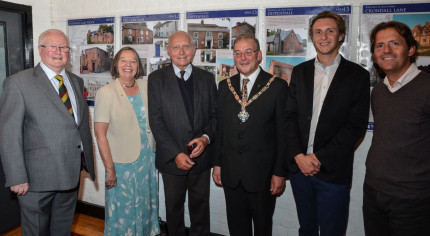 Six people standing in a row in front of an exhibition.