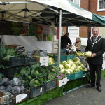 Mayor holds a cauliflower in front of vegetable stall at Food Festival.