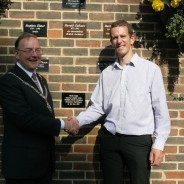 Mayor and man shake hands in front of brick wall after unveiling a commemorative plaque.