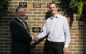 Mayor and man shake hands in front of brick wall after unveiling a commemorative plaque.