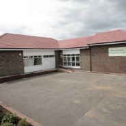 Outside of single storey L shaped community hall. Brick, red tiled roof.