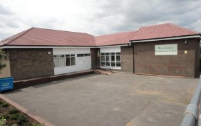 Outside of single storey L shaped community hall. Brick, red tiled roof.