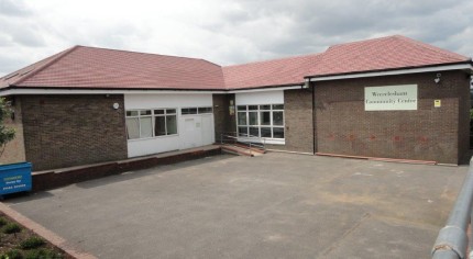 Outside of single storey L shaped community hall. Brick, red tiled roof.