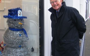 Snowman made from tinsel with blue top hat. shop window. man looking through window at snowman