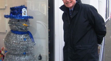 Snowman made from tinsel with blue top hat. shop window. man looking through window at snowman