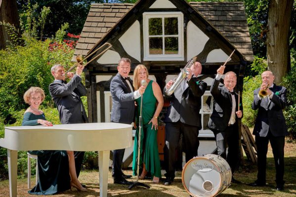 Group of people playing musical instruments in front of a pretty timber cottage