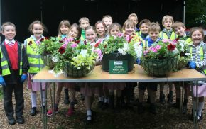 Group of children standing behind a table full of hanging baskets.