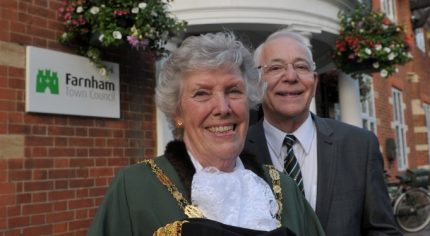 Female Mayor dressed in Mayoral robes and man in suit stand in front of red brick Town Council office.