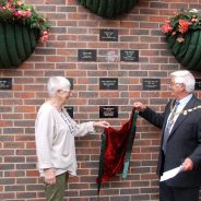 Mayor and female remove a drape to unveil a plaque on a wall.