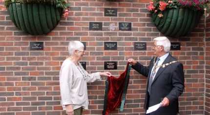 Mayor and female remove a drape to unveil a plaque on a wall.