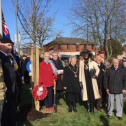 Group of people standing in semi circle. Trees and union flag in background