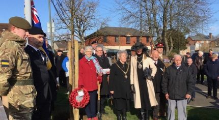 Group of people standing in semi circle. Trees and union flag in background