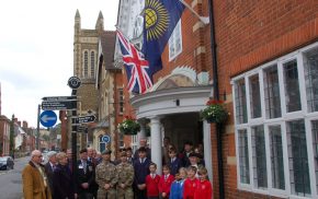 Group of adults and children in front of building. Commonwealth flag and Union flag flying on side of building