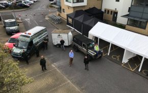 Aerial photo of four people in front of vehicles and a marquee.