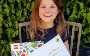 Girl sitting on bench in garden holding a certificate and lego prize.