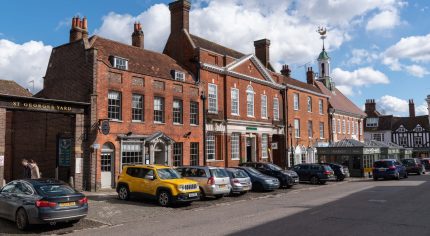 Row of parked cars in front of red bricked shops and businesses. Town centre